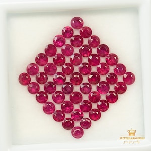 Puede incluir: Una colección de rubíes redondos y facetados de color rojo rosado intenso, dispuestos en forma de diamante dentro de una caja de presentación blanca. La esquina inferior derecha muestra un icono de corona dorada y el texto SUTTIKARNGEMS gems for jewelry.