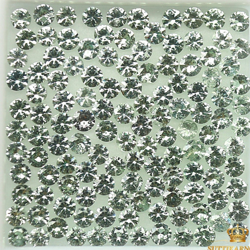 May include: A close-up view of a collection of round, faceted, green gemstones. The gemstones are arranged in a grid pattern on a white background.