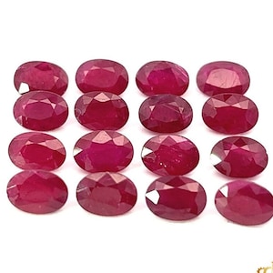 Puede incluir: Una colección de 16 piedras preciosas de rubí de forma ovalada. Los rubíes son de color rojo intenso y tienen un acabado pulido y facetado.