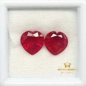 May include: Two heart-shaped red gemstones in a white box. The box has the text "SUTTIKARN GEMs gems for jewelry" on the bottom.