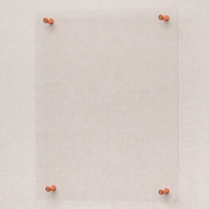 May include: A clear acrylic sign or photo holder, held in place by four copper-colored standoffs. The rectangular display is mounted on a textured, off-white wall, creating a modern and minimalist aesthetic. Ideal for displaying photos, art, or signage.