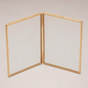 May include: A gold-toned metal picture frame with two hinged panels. The frame is open and ready to display photos.