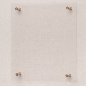 Può includere: Una cornice in vetro trasparente con quattro staffe di montaggio in metallo dorato. La cornice è montata su una parete di colore beige chiaro.