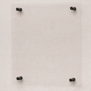 Op de afbeelding: Een helder glazen frame met vier zwarte metalen hoekbevestigingen, gemonteerd op een lichtbeige muur.