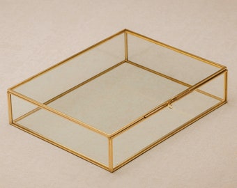 May include: A clear glass box with a gold metal frame and a hinged lid. The box is empty and has a simple design.