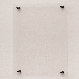 Puede incluir: Un marco de vidrio transparente con cuatro soportes de esquina de metal negro. El marco está montado en una pared de color beige claro.