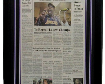 May include: A framed newspaper clipping from the Los Angeles Times, dated June 16, 2001, with the headline "To Repeat: Lakers Champs". The image shows a basketball player holding a champagne bottle and celebrating. The newspaper also includes articles about a tough scene for actors, bishops banning sterilization services, and a power debate.