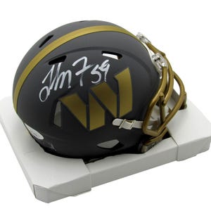 May include: A black football helmet with gold accents, including a stripe and face mask. The helmet features a gold "W" logo and a handwritten signature with the number "59". The helmet rests in a white cardboard holder.