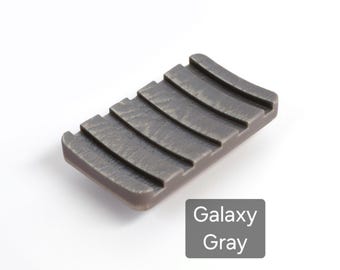 Jabonera con patas antideslizantes y textura de madera. Diseño con forma de pala que atrapa el agua.