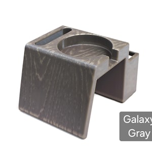 Puede incluir: Un portavasos gris galaxia con una apariencia de vetas de madera texturizada. El portavasos tiene una abertura circular para una taza, una ranura para un tel&eacute;fono y una peque&ntilde;a abertura rectangular. El producto est&aacute; hecho de un material duradero.