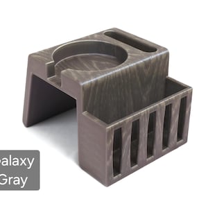 Puede incluir: Un organizador de escritorio Galaxy Gray con un portavasos, una ranura y un peque&ntilde;o compartimento rectangular con listones verticales. El organizador est&aacute; hecho de un material similar a la madera y tiene un aspecto texturizado. El texto "Galaxy Gray" est&aacute; en un cuadro gris.