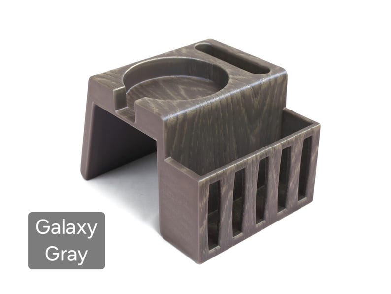 Puede incluir: Un organizador de escritorio Galaxy Gray con un portavasos, una ranura y un peque&ntilde;o compartimento rectangular con listones verticales. El organizador est&aacute; hecho de un material similar a la madera y tiene un aspecto texturizado. El texto "Galaxy Gray" est&aacute; en un cuadro gris.