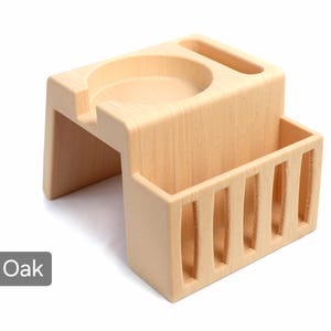Puede incluir: Un organizador de escritorio de madera de roble de color claro con un portavasos incorporado, una ranura y un compartimento de almacenamiento rectangular con listones verticales. La palabra "Oak" est&aacute; en un cuadro gris en la esquina inferior izquierda.