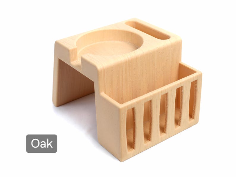 Puede incluir: Un organizador de escritorio de madera de roble de color claro con un portavasos incorporado, una ranura y un compartimento de almacenamiento rectangular con listones verticales. La palabra "Oak" est&aacute; en un cuadro gris en la esquina inferior izquierda.