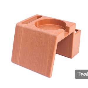 Puede incluir: Un organizador de escritorio color teca con un portavasos circular, una peque&ntilde;a ranura rectangular y un compartimento lateral. El organizador tiene un aspecto de veta de madera texturizada y est&aacute; etiquetado como "Teca".