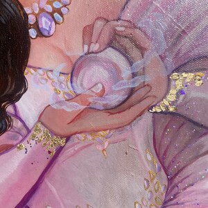 May include: A close-up of a hand holding a small, round, purple orb. The orb is surrounded by a white, wispy smoke. The hand is wearing a pink and gold bracelet.
