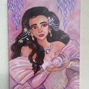 May include: A painting of a woman with long dark hair wearing a pink dress and holding a pearl in her hands. She is adorned with gold jewelry and flowers. The background is a soft pink with purple and gold accents.