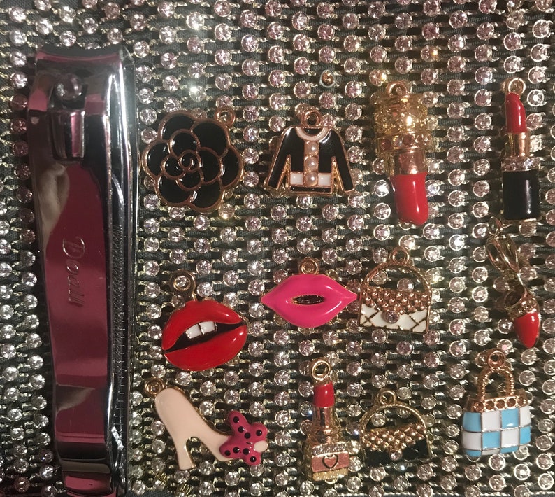May include: A close-up of a variety of charms, including a black and white Chanel-inspired charm, a red lipstick charm, a red and white striped charm, and a black and white checkered charm. The charms are all attached to a silver chain.