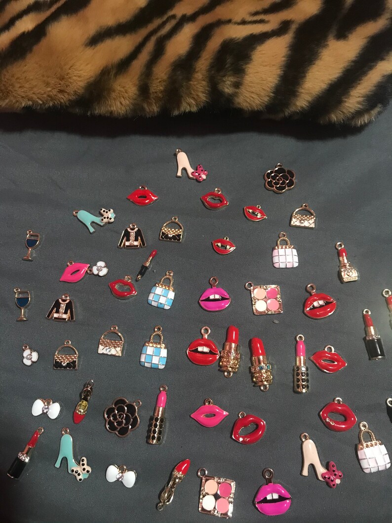 May include: Assortment of colorful enamel charms featuring various fashion and beauty themed designs.  The charms include lips, purses, shoes, lipstick, wine glasses, and makeup palettes.  The charms are all gold-toned and have a shiny finish.