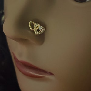 May include: A gold nose ring with a double heart design and a clear stone in the center.