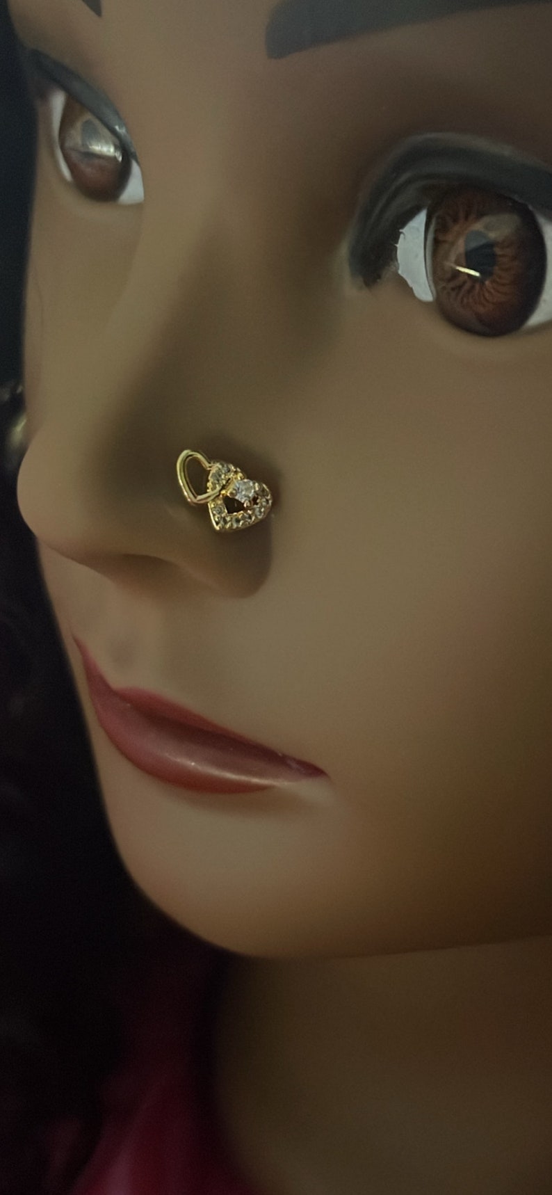 May include: A gold nose ring with a double heart design and a clear stone in the center.