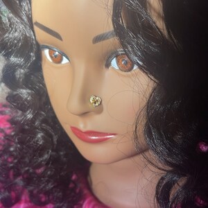 May include: A close-up of a mannequin's face with long, dark curly hair. The mannequin is wearing a gold heart-shaped nose ring.