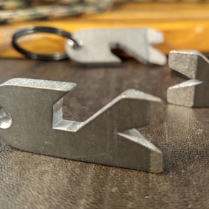 以下が含まれることがあります： 異なる形のツールが付いた銀色の金属製のキーホルダーが3つ。キーホルダーは茶色の革の表面にあります。