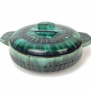 May include: A green ceramic casserole dish with a lid and two handles. The dish has a mottled green glaze with a darker green rim.