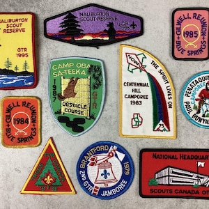 Op de afbeelding: Een verzameling vintage geborduurde patches met diverse ontwerpen en tekst. Patches bevatten teksten als "Haliburton Scout Reserve", "Camp Oba Sa-Teeka" en "Centennial Hill Camporee". Kleuren zijn rood, geel, groen en blauw. Deze patches zijn waarschijnlijk van scoutingevenementen.