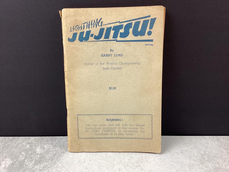 May include: Vintage "Lightning Ju-Jitsu!" book with blue text on a tan cover. The book, by Harry Lord, details Judo techniques. A warning about the secret instructions is printed at the bottom. The book is a collectible item.