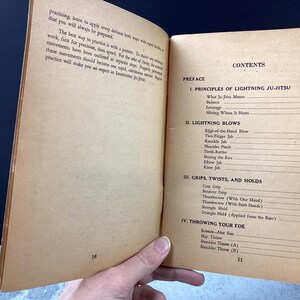 May include: Open book with aged, tan pages. The right page displays the "CONTENTS" with sections like "PRINCIPLES OF LIGHTNING JU-JITSU" and "LIGHTNING BLOWS." The left page has text about practicing and applying defense.