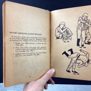 May include: Open book page with text and illustrations about sentry defense against mugging. The text describes techniques, accompanied by three black and white illustrations showing the steps. The book is held open by a hand.