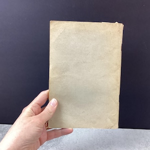 May include: A rectangular, aged paper item with a light tan color. The paper has visible wear and tear, with slightly curled edges. The item is held by a hand, suggesting its size and scale.