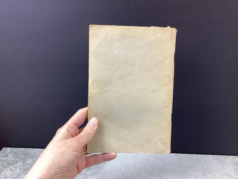 May include: A rectangular, aged paper item with a light tan color. The paper has visible wear and tear, with slightly curled edges. The item is held by a hand, suggesting its size and scale.