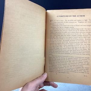 May include: Open book with aged, yellowed pages. The text, "A FOREWORD BY THE AUTHOR," is visible at the top of the right-hand page. The book is held open by a hand, revealing the text of the foreword.