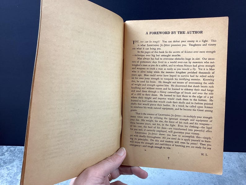 May include: Open book with aged, yellowed pages. The text, "A FOREWORD BY THE AUTHOR," is visible at the top of the right-hand page. The book is held open by a hand, revealing the text of the foreword.