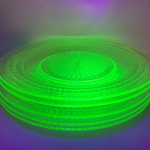 May include: A stack of four green glass plates with a decorative pattern. The plates are made of uranium glass, which gives them a distinctive green colour.