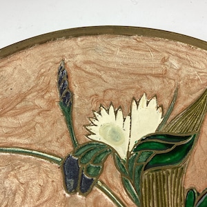 Puede incluir: Un plato decorativo con un dise&ntilde;o floral. El plato presenta un fondo rosa claro y un borde dorado. Las flores son blancas con hojas y tallos verdes. El dise&ntilde;o es detallado e intrincado.