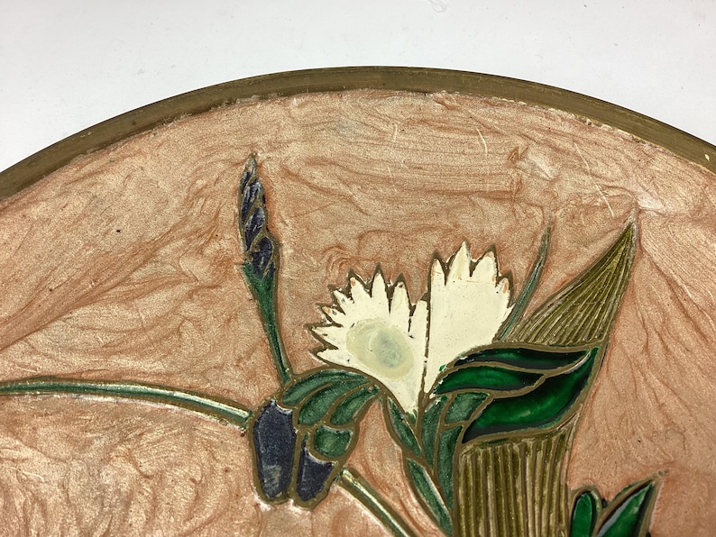 Puede incluir: Un plato decorativo con un dise&ntilde;o floral. El plato presenta un fondo rosa claro y un borde dorado. Las flores son blancas con hojas y tallos verdes. El dise&ntilde;o es detallado e intrincado.