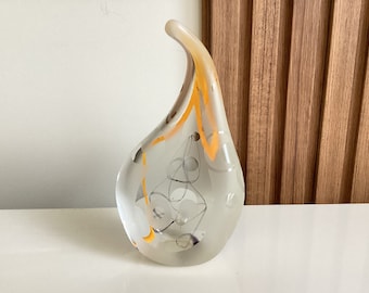 May include: A clear glass sculpture with a teardrop shape and a long, curved neck. The sculpture has a swirl of yellow and white paint on the outside and a design of black and white circles and lines on the inside.