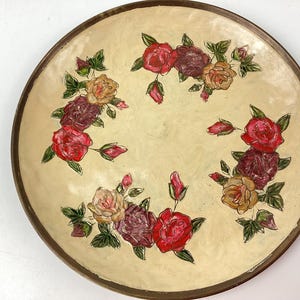 Puede incluir: Plato decorativo redondo con superficie color crema y borde marr&oacute;n oscuro. El plato est&aacute; adornado con rosas pintadas a mano en tonos rojos, burdeos y amarillos, con hojas verdes. Una pieza de estilo vintage.