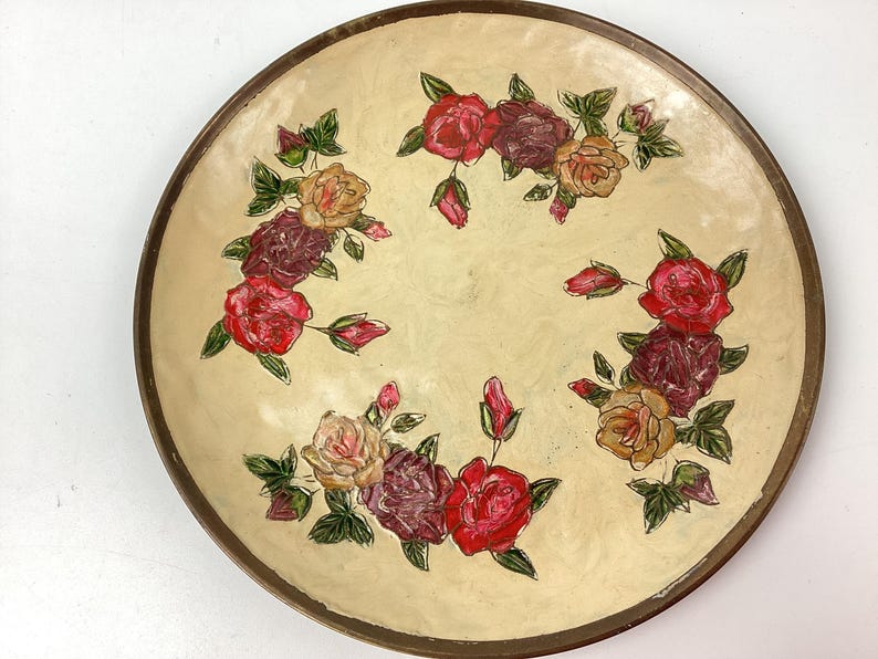 Puede incluir: Plato decorativo redondo con superficie color crema y borde marr&oacute;n oscuro. El plato est&aacute; adornado con rosas pintadas a mano en tonos rojos, burdeos y amarillos, con hojas verdes. Una pieza de estilo vintage.