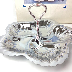 May include: A silver serving tray with a handle, shaped like a flower with four petals. The tray has a wavy, textured surface.