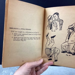 May include: Open book page with text "BREAKING A FULL-NELSON" and instructions on how to break a full-nelson wrestling hold. Includes black and white illustrations of the wrestling move. The page is aged with a yellowed tone.