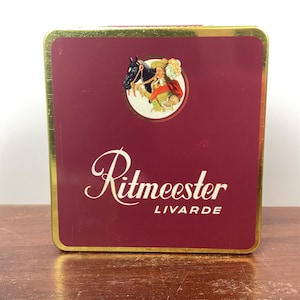 May include: A red and gold tin box with a gold trim. The box has a picture of a man on a horse and the text "Rittmeester Livarde" on the front.