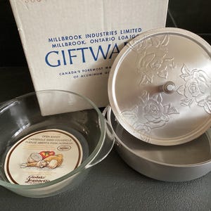 以下が含まれることがあります： 蓋にバラの模様が施された銀色のアルミニウム製のベーキングディッシュ2個セット。小さい方の皿は透明なガラス製です。箱には「ギフトウェア」と「カナダで最も有名なアルミニウム製品メーカー」と書かれています。