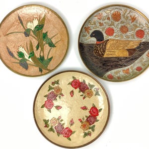 Puede incluir: Tres platos redondos decorativos con dise&ntilde;os florales y de animales. Uno presenta un pato, otro flores y el tercero un dise&ntilde;o floral y vegetal. Cada plato tiene un borde dorado.