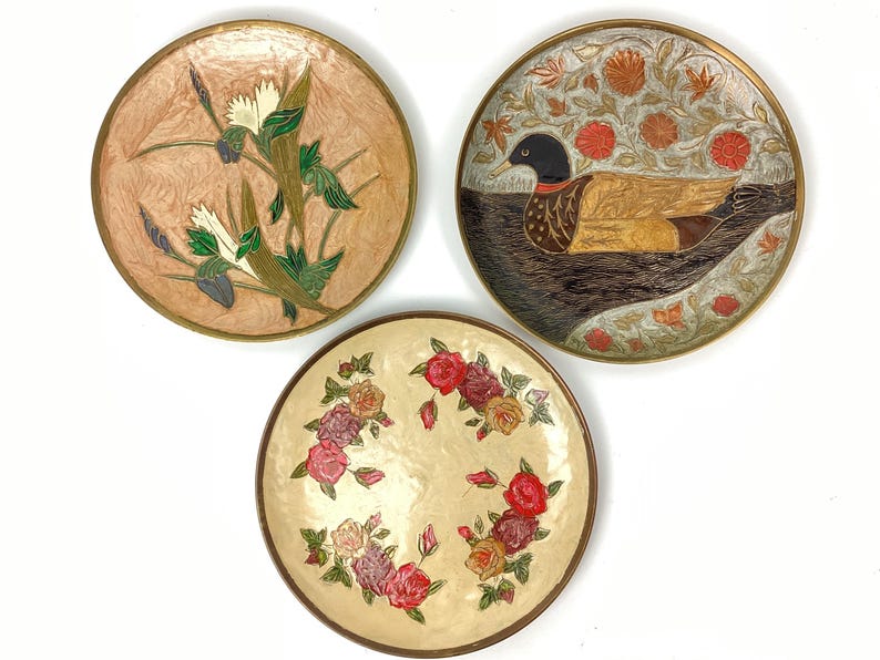 Puede incluir: Tres platos redondos decorativos con dise&ntilde;os florales y de animales. Uno presenta un pato, otro flores y el tercero un dise&ntilde;o floral y vegetal. Cada plato tiene un borde dorado.