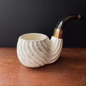 May include: White ceramic pipe planter with a black and gold rim. The planter is shaped like a pipe and has a textured, swirl design.