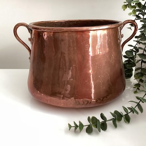 Peut inclure: Une grande casserole en cuivre avec deux anses. La casserole a une finition martelée et est légèrement bosselée.
